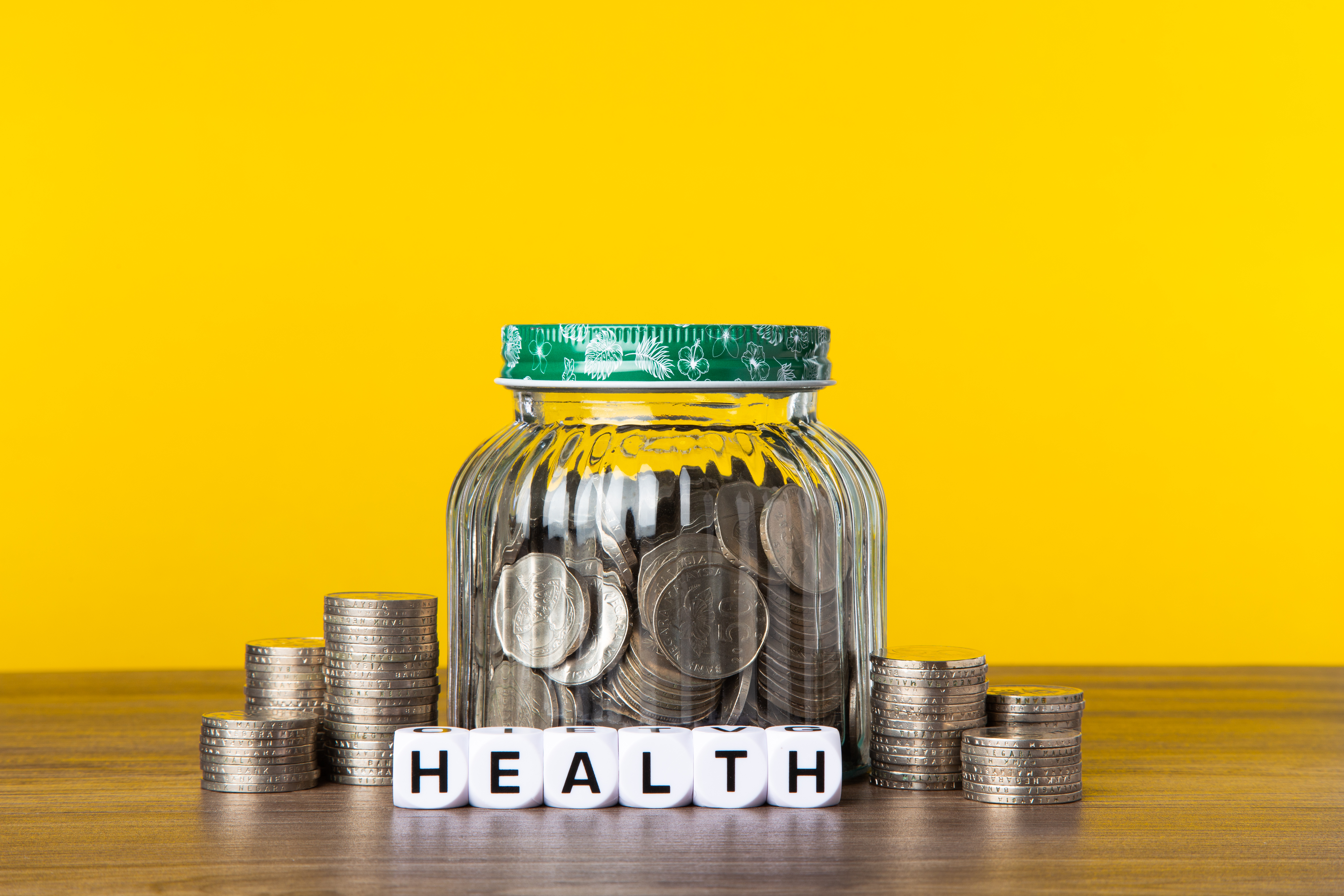 A lot coins in glass money jar with yellow background. Saving for Health concept.