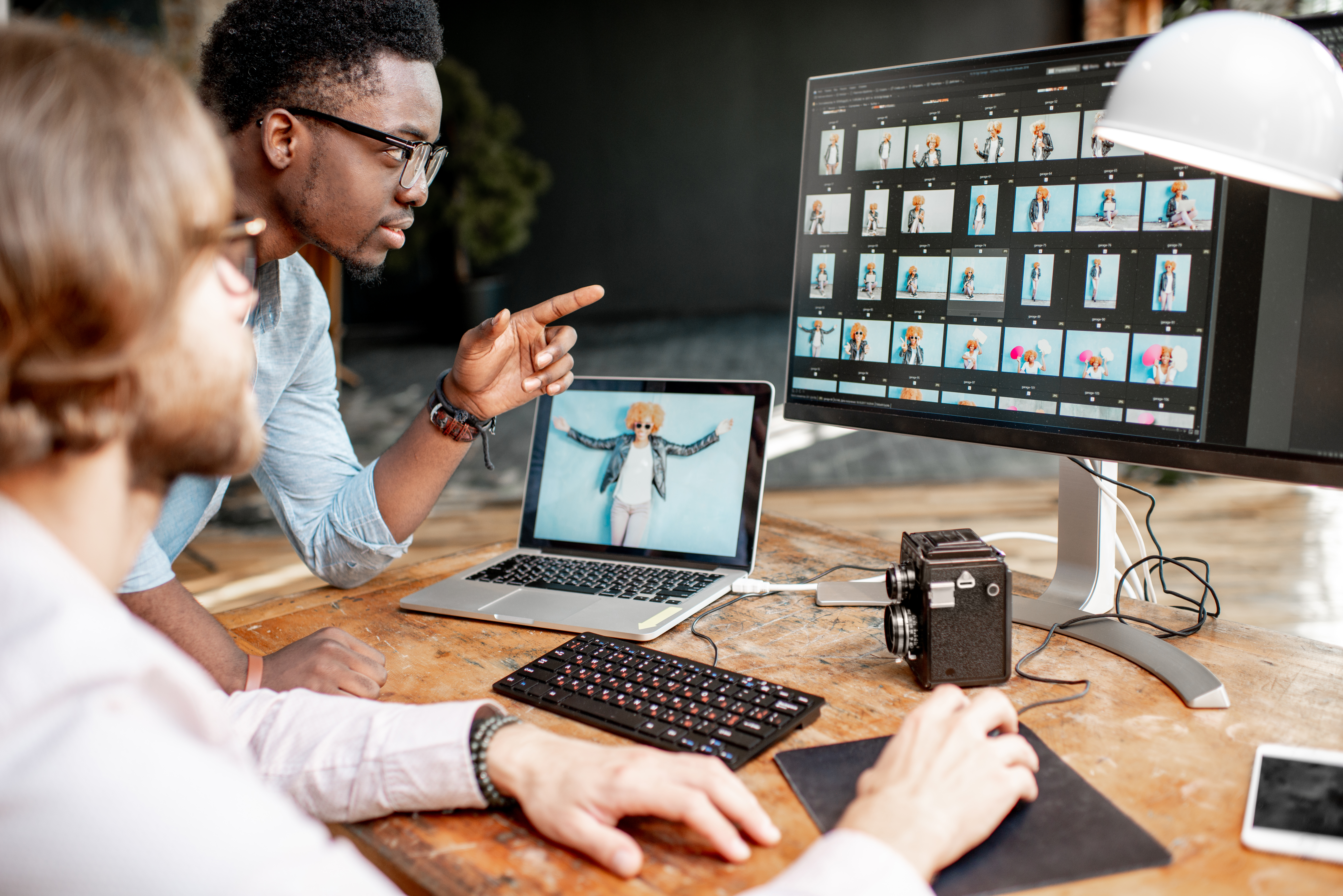 Two male photographers choosing woman's portraits at the working place with two computers in the studio